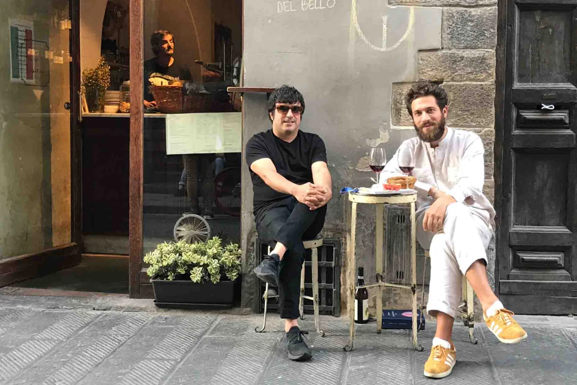 To menn nyter et glass vin ved et lite bord på gaten