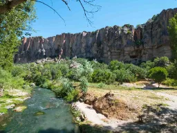 Elv i den frodige Ihlara-dalen med bratte fjellvegger i bakgrunnen under blå himmel Elv i den frodige Ihlara-dalen med bratte fjellvegger i bakgrunnen under blå himmel
