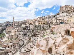 Uchisar-slottet i Kappadokia reiser seg over byen, omgitt av hus og huler hugget ut i de myke klippene Uchisar-slottet i Kappadokia reiser seg over byen, omgitt av hus og huler hugget ut i de myke klippene