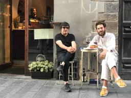 To menn nyter et glass vin ved et lite bord på gaten