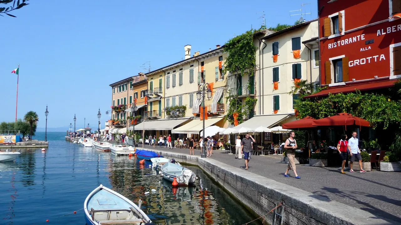 Havnen i Lazise ved Gardasjøen med båter, promenade og historiske bygninger langs vannet Havnen i Lazise ved Gardasjøen med båter, promenade og historiske bygninger langs vannet