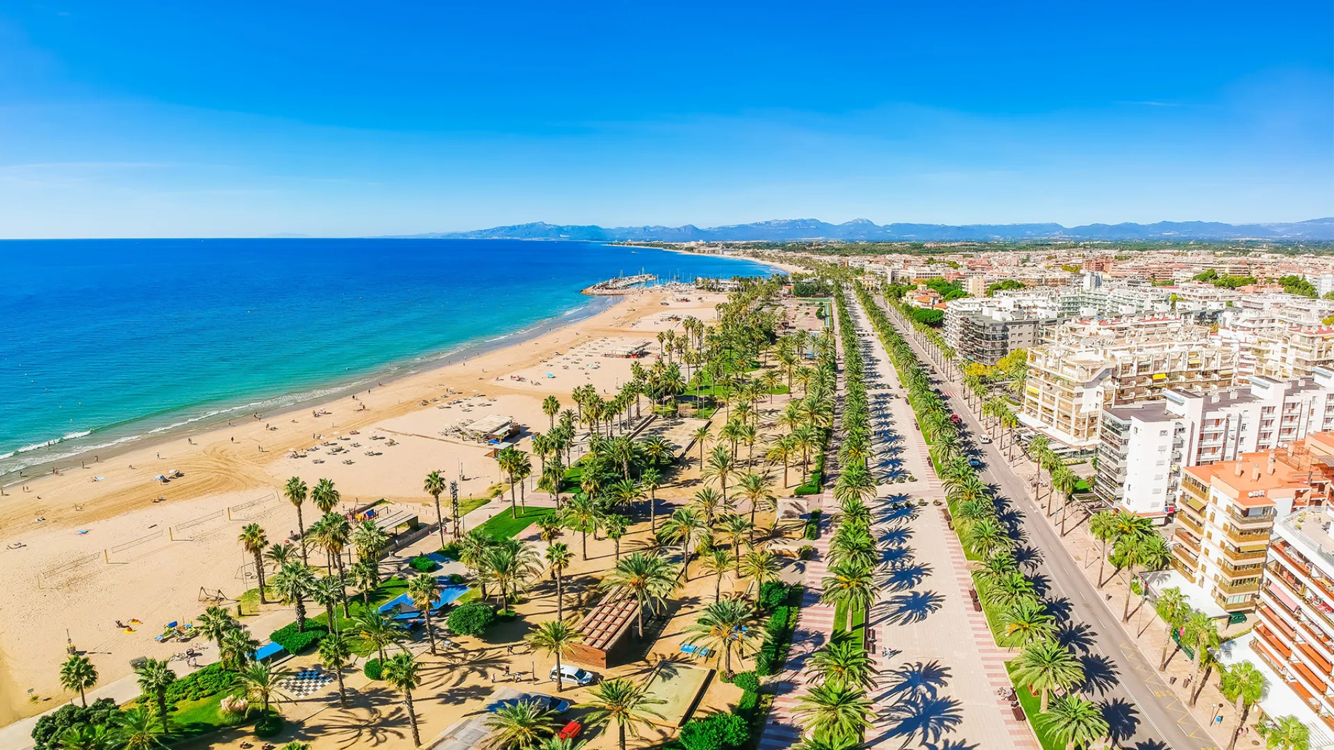 Hoteller, palmer, strand, turkisblått hav, solskinn og fjell i bakgrunnen Hoteller, palmer, strand, turkisblått hav, solskinn og fjell i bakgrunnen